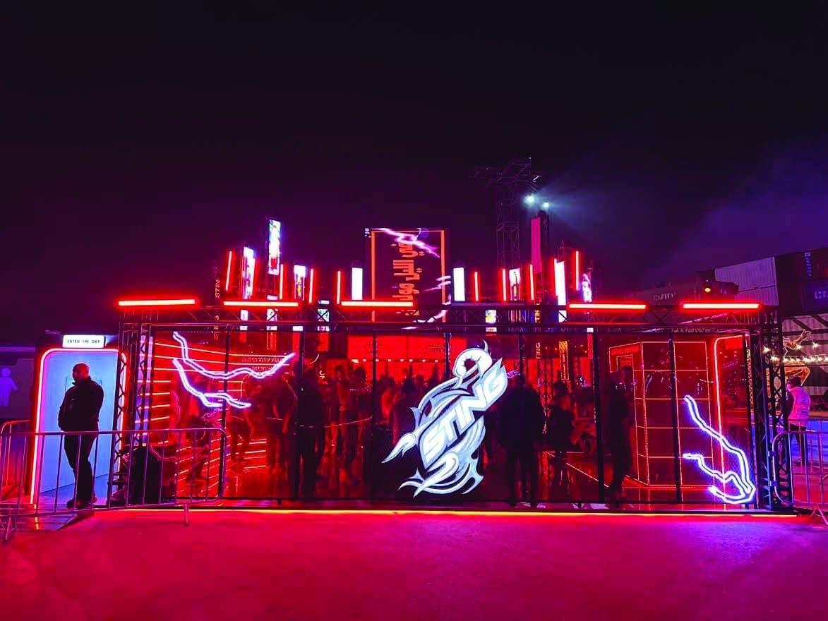 An outdoor brand activation lit in neon red at night, with visitors moving through the structure