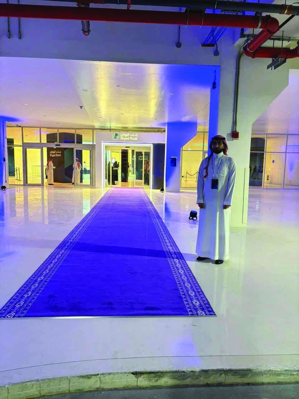 A blue carpet arrival route leading to the entrance of an event venue, with a host waiting beside it